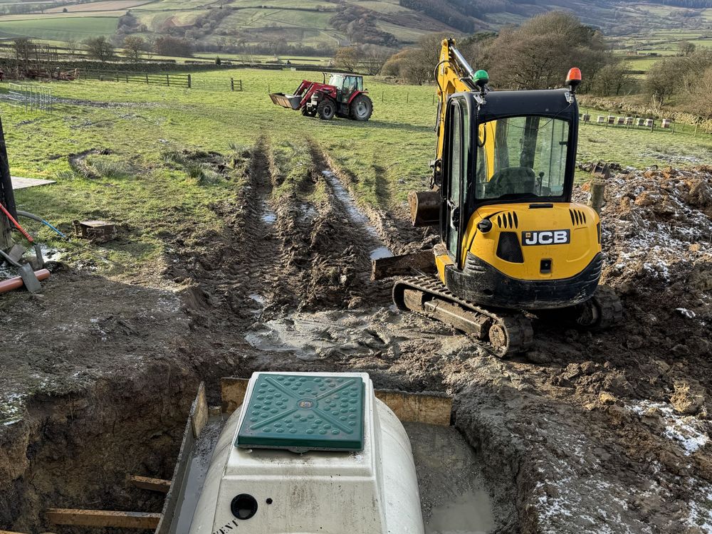 New sewage treatment tank set into its excavation on a farm, with a mini digger working beside it